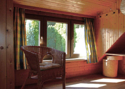 Rustikale Sitzecke im Obergeschoss des Ferienhauses Meyer mit Rattanstuhl, Holzambiente und Blick in den Garten