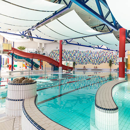 Innenansicht des Marienbads in Bad Marienberg mit großem Schwimmbecken, Wasserfontäne und roter Rutsche