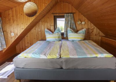 Gemütliches Schlafzimmer unter dem Dach im Ferienhaus Meyer, ausgestattet mit einem Doppelbett, gestreifter Bettwäsche und holzverkleideten Wänden