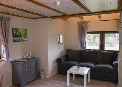 Gemütlichen Wohnzimmers mit einem grauen Sofa, einem weißen quadratischen Couchtisch, einer grauen Kommode und einem Wandbild mit einer Waldszene im Ferienhaus Meyer.