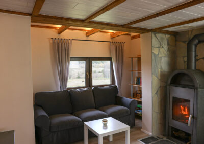 Gemütlicher Wohnbereich im Ferienhaus Meyer mit grauem Sofa, weißem Couchtisch und einem brennenden Kamin vor einer Steinwand