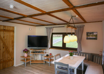 Essbereich mit weißem Tisch, Stühlen und Eckbank sowie ein TV-Bereich mit Fernseher auf einem Regal in einem gemütlichen Wohnraum des Ferienhauses Meyer
